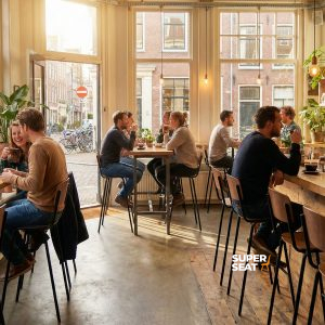 Super-Seat | Mensen zitten aan bruine houten tafels en Vanitas barkrukken in een licht, gezellig café met veel ramen en planten. |. | Horecameubilair