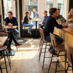 Super-Seat | Barhocker aus cognacfarbenem Leder und Metall an Holztischen in einem Café mit Backsteinwänden und viel Licht. | Catering Möbel