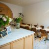 Super-Seat | Cafe Interieur | Ein Cafe mit braunen/eichen Holzstühlen und weißen runden Tischen, einem Marmortresen, weißen Wänden und einem gesprenkelten Boden. | Catering Möbel