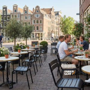 Super-Seat | Schwarze Stapelstühle und Tische aus Metall auf einer Klinkerterrasse mit Pflanzen und Blick auf die Stadt. | Catering Möbel