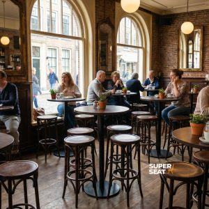 Super-Seat | Zwarte ronde statafels, houten stoelen, grote ramen, planten, warme sfeer in café. | Horecameubilair