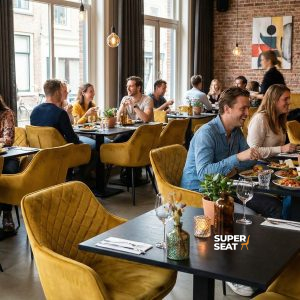 Super-Seat | Diamond fluwelen horeca stoelen oker | Fluwelen okergele stoelen en houten tafels sieren het modern restaurant met planten en grote ramen. | Horecameubilair