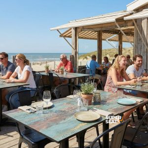 Super-Seat | Terrassentischplatten Rost und Kupfer Braune HPL-Tische 70x70cm, Terrassenboden aus Holz umgeben von Strand, Stühle in neutralen Tönen. | Catering Möbel