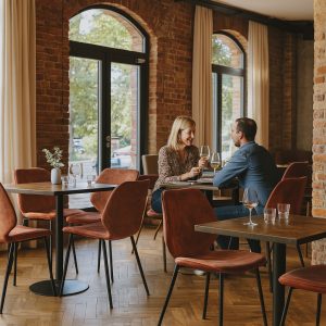 Super-Seat | Eine Frau und ein Mann sitzen an einem Tisch in einem modernen Restaurant mit Backsteinwänden und genießen Wein. | Zwarte vintage lederstoelen met schelpvorm, op metalen poten naast houten tafels; industrieel en stijlvol. | Horecameubilair