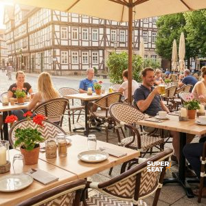 Super-Seat | Beigefarbene Boho-Stühle mit Armlehnen, Holztische, Barhocker, cremefarbene Sonnenschirme, Platz mit Kopfsteinpflaster. | Catering Möbel