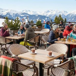 Super-Seat | Boho beige Stühle mit Armdecken, Holztische und Hocker auf verschneiter Terrasse, Menschen in Winterkleidung. | Catering Möbel