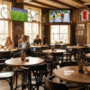 Super-Seat |Tische, Stühle und Barhocker aus Holz; warme Eichenfarbe in der Sportbar mit Fahrrädern an der Wand. | Catering Möbel