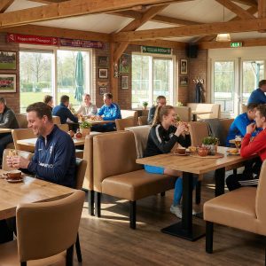 Super-Seat | Lisa hospitality Esszimmerbank Bistro Taupe - 120cm | Taupe Esszimmerbank mit Holztisch, Metallstühlen in hellem Café mit Sportdekor und Holzbalken. | Catering Möbel