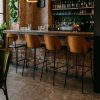 Super-Seat | Eine Bar mit einem Steinboden, einer Ziegelwand und vier New Yorker Designer-Barhockern aus schwarzem Leder. | Vier schwarze Lederbarhocker mit Holzbeinen; Bar mit Steinboden und Innenwand. | Catering Möbel