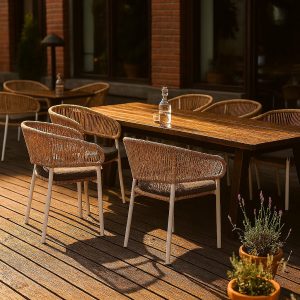 Super-Seat | Ein hölzerner Esstisch für draußen mit sechs Ibiza wit (terras) stapelstoelen met kussen | Lichtbruine houten tafel, witte kunststof stapelstoelen met grijze kussens, glazen fles, planten. | Horecameubilair