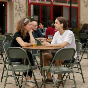 Super-Seat | Zwei Personen sitzen an einem Tisch im Freien mit Getränken | Armeegrüne Metall-Klappstühle, Holztisch, Industriële look, rode raamkozijnen. | Horecameubilair